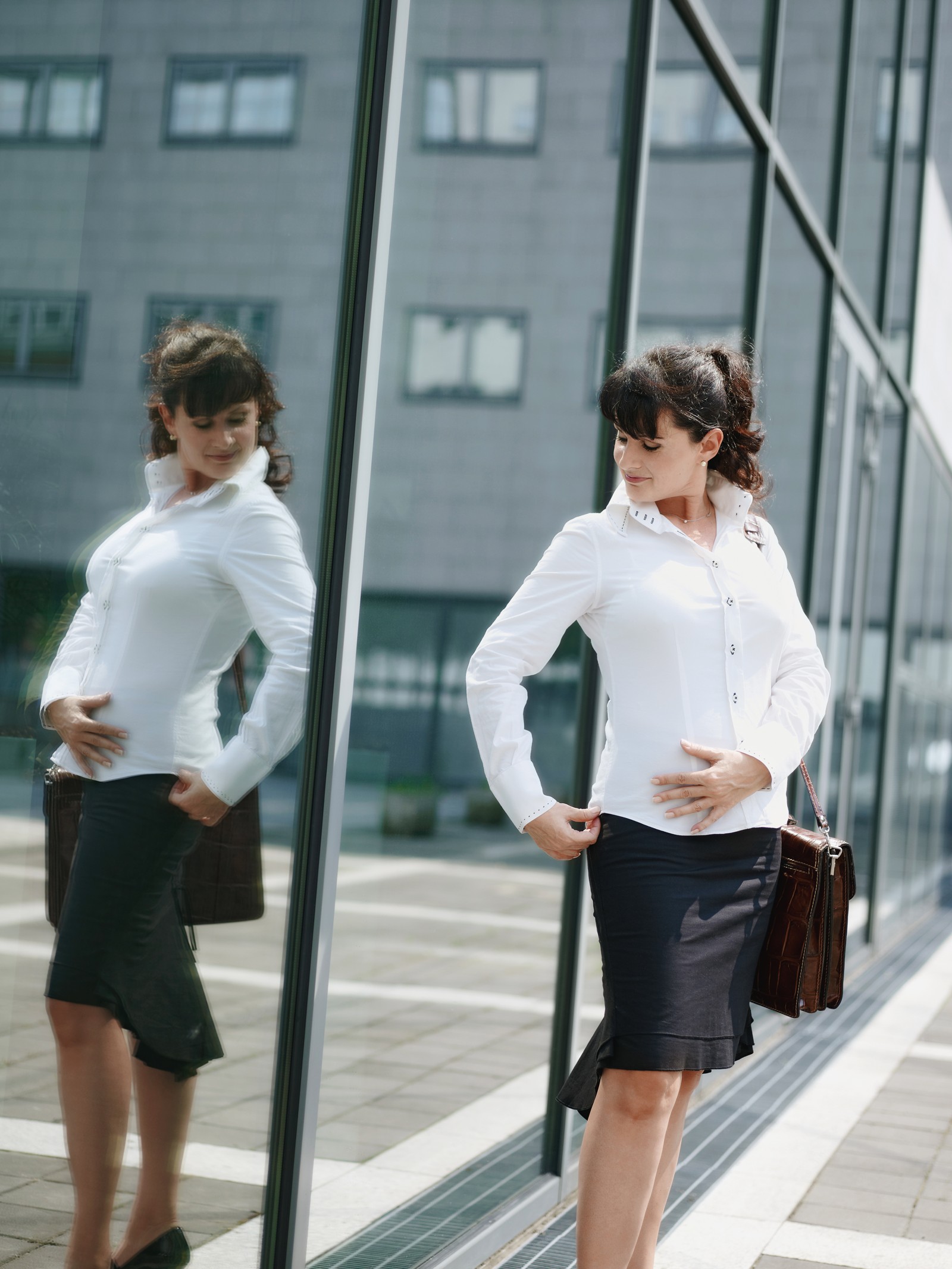 A woman standing beside a glass building, with her reflection visible alongside her.